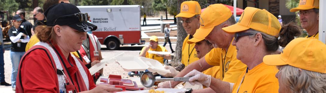 Photo of Disaster Relief Arizona volunteers wearing yellow orange shirts and hats, serving fellow volunteers (Red Cross), and citizens at the Individual Assistance Service Center (IASC).